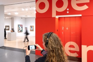 An image of a woman taking an audio/visual tour of a museum with a pair of headphones connected to a smart phone