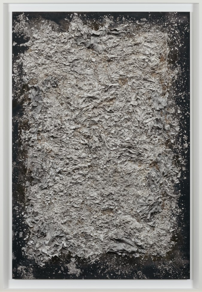 Color image of a color photograph depicting a neat pile of burnt documents on black background framed in white