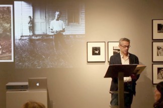 Video still of a man standing at a podium in a gallery