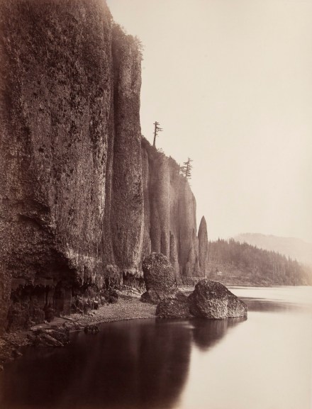 Color photograph of a cliffside and water with trees on horizon