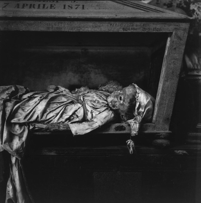 Black-and-white photograph of a preserved child's body lying in a wooden compartment