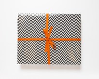 Color image of a wrapped box with black and white zigzag wrapping paper and an orange bow