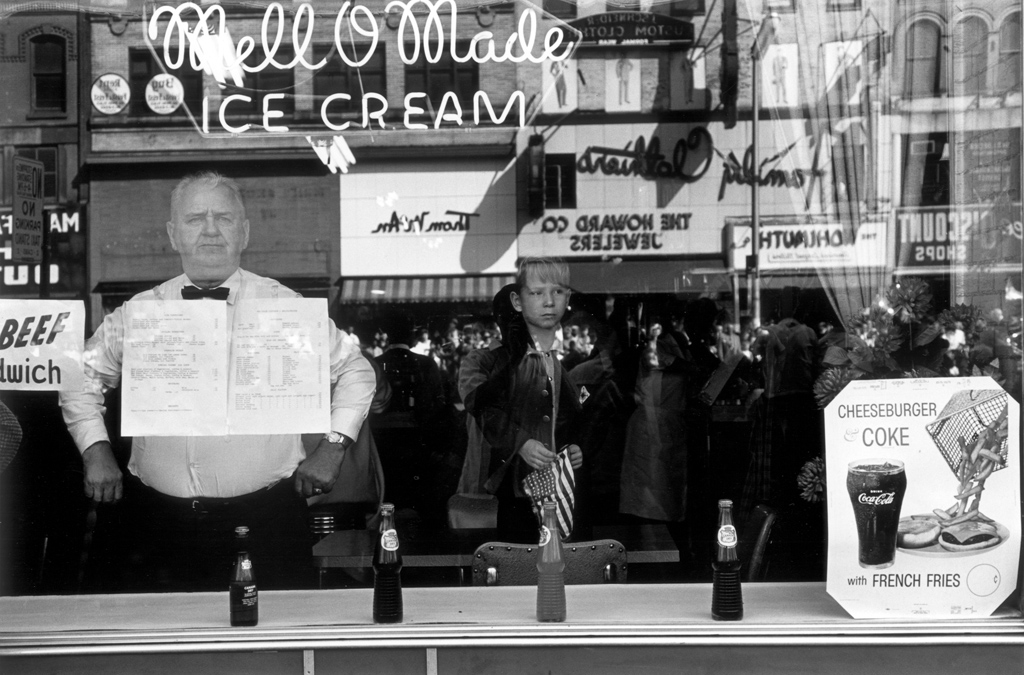 Black-and-white photograph of a man looking out the window of an ice cream parlour