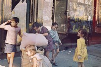 Color photograph of five young children on a city sidewalk before a graffitied storefront