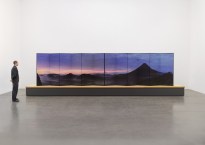 Installation view of a person standing in a gallery next to a long folding screen depicting Mt. Fuji; the screen sits on a large pedestal