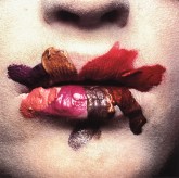 Color photograph of a mouth up close smeared with varying shades of red lipstick