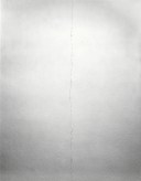 Black and white photograph of a long straight crack in a white wall