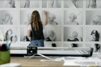 Color photograph of a person making notes on prints in an art studio