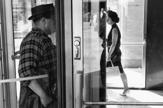 Black-and-white photograph of a man and woman entering and exiting a building with their faces obscured by doors