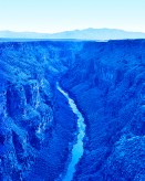 Color photograph of a gorge with mountains on the horizon entirely in a blue tone
