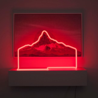 Collage of an etched print and photograph of a mountain outlined by red neon light on a shelf in front of it