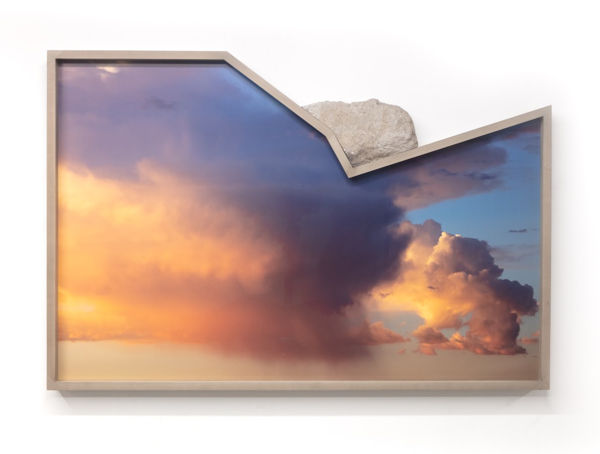 Color image of a color photograph of a cloudy sky with shades of pink and blue and a rock resting on frame on white background