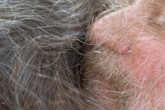 Close up color photograph of a bearded person's face resting in another person's hair
