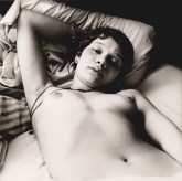 Black and white photograph of nude woman in reclining in bed