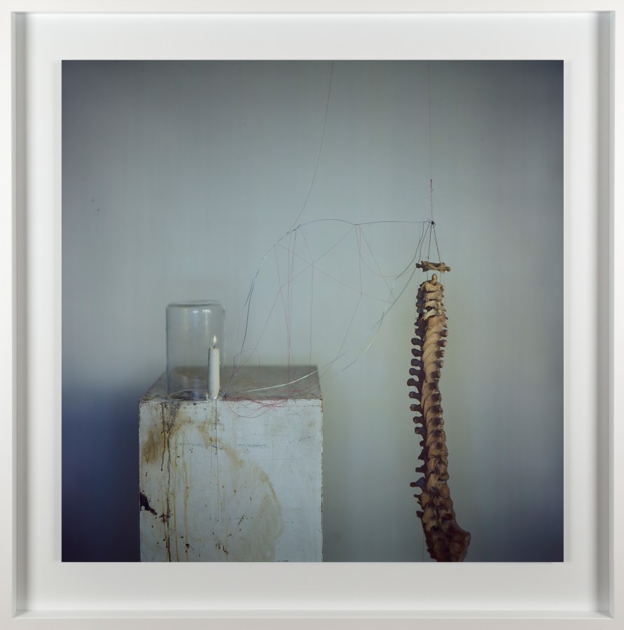 Color photograph of a lit candle and glass jar on a stone plinth next to a vertebrae