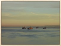 Color photograph framed in bleached wood depicting several cargo ships on the water close to sunset
