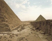 Color photograph of a lone figure looking up at a pyramid