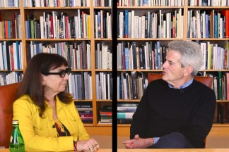 Color video still of two seated figures in a library talking