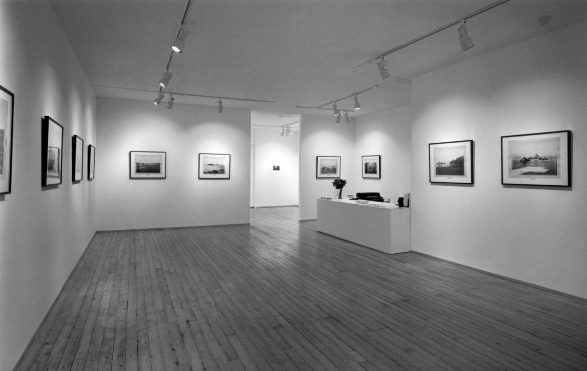 Black-and-white photograph of a gallery interior with works framed on the walls.